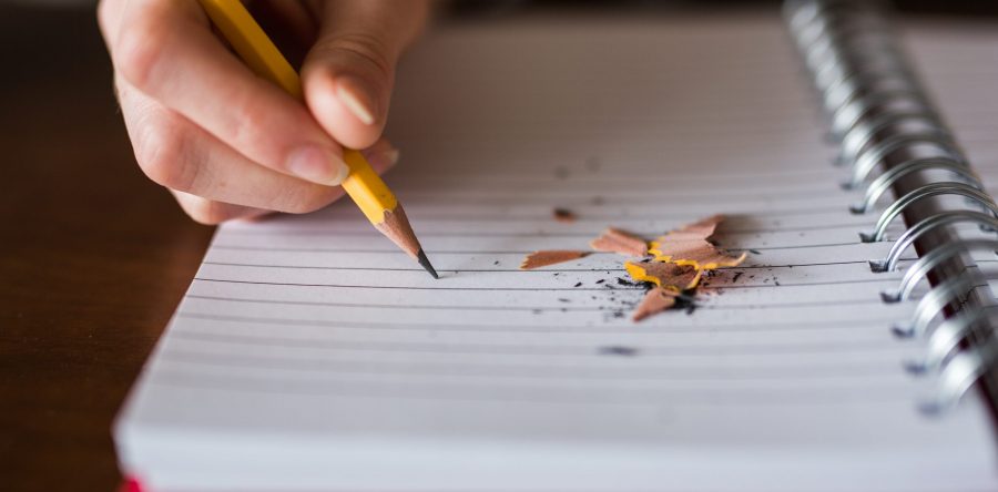 Teaching assistant writing on paper with pencil sharpenings next to pencil